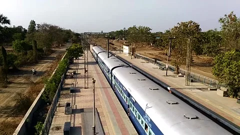 Long Indian Passenger express train crossing scenic Umroli railway station India Stock Footage 140633496