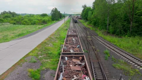 Long line of scrap wagons stretches along rails beside green country road Stock Footage 319953130