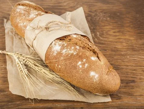 Long loaf in paper packaging with ears of wheat Stock Photos