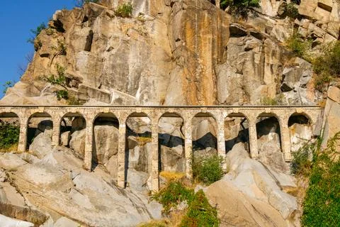 Long masonry arcade with repeating arches built into a rocky cliff face, st.. Stock Photos