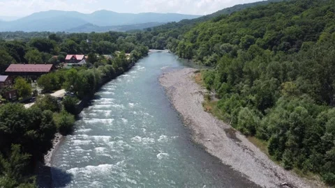 A long mountain river flows through a small settlement. Aerial view. Video stock 332211951