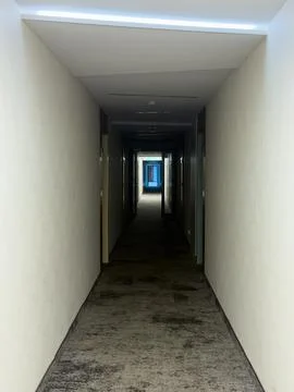 Long narrow corridor inside hotel with bright door at end Stock Photos