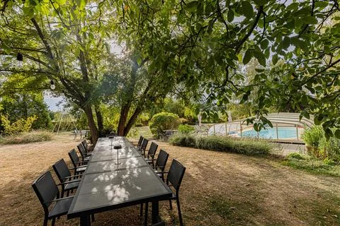 Long outdoor dining table beneath mature trees beside the pool at Chateau d.. Stock Photos