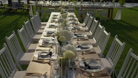 Long outdoor wedding table with white roses and gold cutlery on lawn 動画素材 344512169