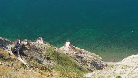 A long path down with many steps from high mountains and cliffs to the sea with  Stock Footage 115425710