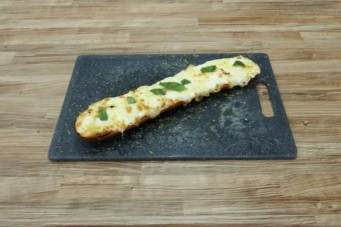 A long piece of bread with cheese and herbs on top Foto stock