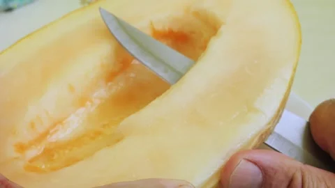 Long pieces are cut off from a melon cut lengthwise with a knife. Medium shot Stock Footage 289006715