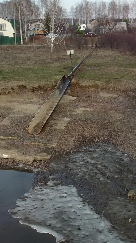 Long pipe lies broken in muddy ditch near ice-capped pond Stock Footage 347499208
