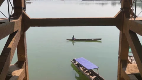 A long pirogue passes under a concrete bridge on a lake in Laos Stock Footage 236574096