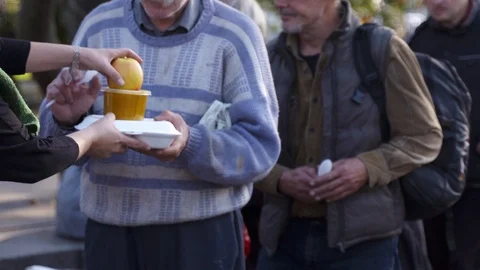 Long queue for free food. Volunteers giving fruit to the poor people Stock Footage 117347344