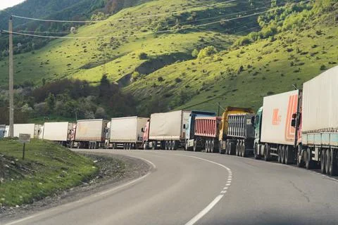Long queue of trucks delivering products standing over picturesque mountain view Stock Photos
