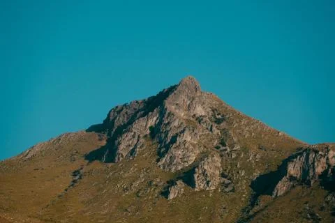 A long range shot of a mountain with dry grass field and a blue sky in the ba Stock Photos