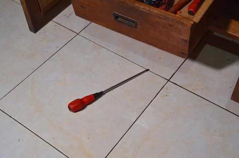 A Long Red Handled Screwdriver Resting On A Light Tiled Floor Near An Open .. Fotos de archivo