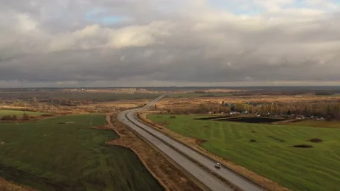 A long road passes through green fields over which low gray clouds float through Stock Footage 172347814