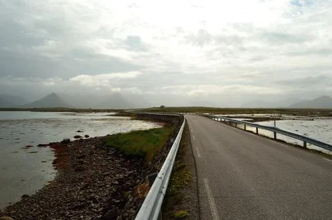 Long road through flat landscape with mountain in background and ocean on sid Foto stock