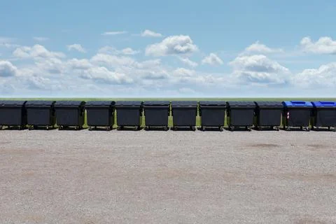 Long row of black garbage containers outside under the blue sky Stock Photos