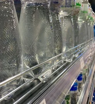 Long rows of bottles of drinking water on the shelf of a convenience store Stock Photos