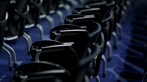 Long rows of empty modern chairs with metal armrests in a dimly lit auditorium Stock-Footage 325669327