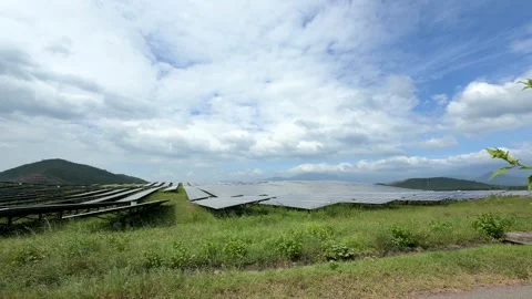 Long rows of solar panels stretch toward rolling hills beneath drifting clouds Stock Footage 325659928