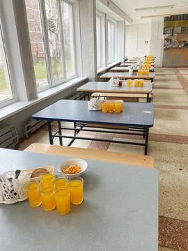 Long rows of tables in a school cafeteria with orange juice glasses and snacks Stock Photos