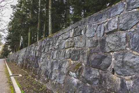 A long, rustic stone retaining wall stretches along a forested path. Stock Photos