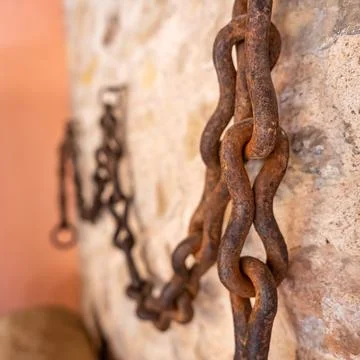 Long rusty chain placed on the stone wall for field work in the village of Stock Photos