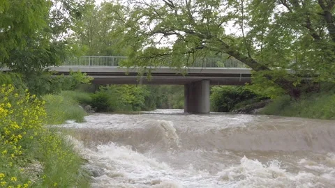 Long sequence of muddy highwater river with a bridge while tilting down in Video stock 136223495