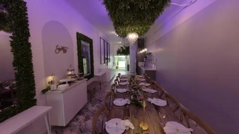 Long set dining table under chandeliers in a purple-lit room Stock Footage 345565098