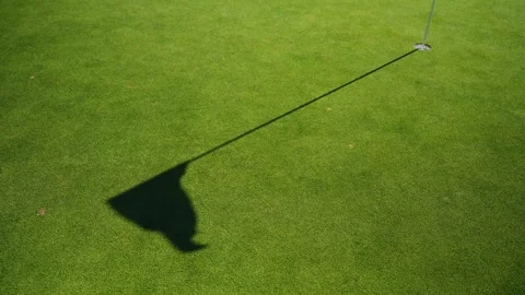 Long shadow of a flagstick stretches across a manicured green as it waves in Stock Footage 329003512