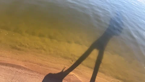 Long Shadow of Person Walking with Bag Along Quiet Waters Edge Stock Footage 340280549