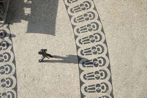 Long shadows of people on a square with pattern of paving stones Stock Photos