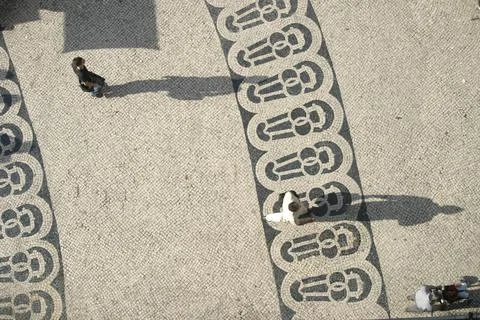 Long shadows of people on a square with pattern of paving stones Stock Photos