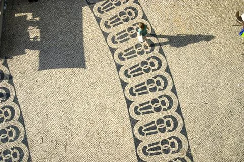 Long shadows of people on a square with pattern of paving stones in Lisbon ph Stock Photos