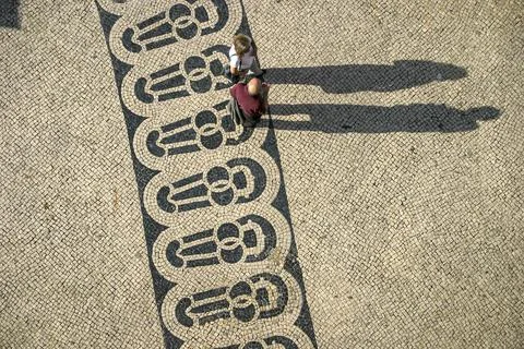 Long shadows of people on a square with pattern of paving stones Stock Photos