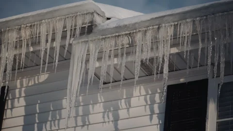 Long, sharp icicles hanging from the edge of a snow-covered roof on a cold Vidéo 323460884