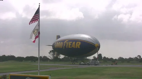 Long shot of Good Year Blimp with American flag in foreground Stock Footage 6635035