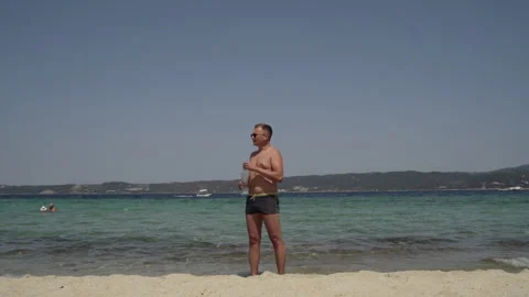 Long shot of a man at the beach. Man in sunglasses, in swimsuit, drinking water Stock Footage 147948727