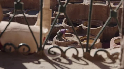 Long shot of tannery leather worker dyeing white leather in Fes through grill Stock Footage 265490800