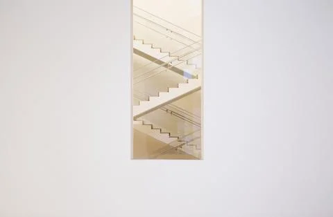 Long shot of zig zag staircase through window in white wall. Stock Photos