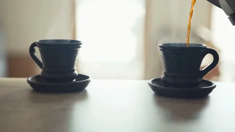 Long slow motion footage of steaming hot coffee pouring into two black clay cups Video stock 118934591