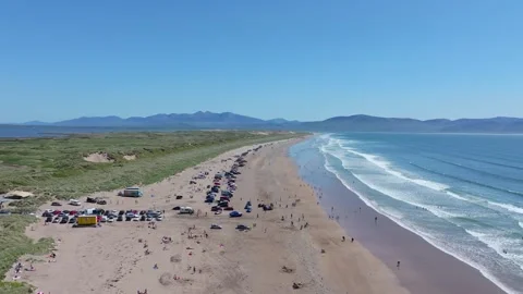 Long Stretch of Sandy Beach with Visitors and Parked Cars on a Clear Day Stockbeeldmateriaal 337036939