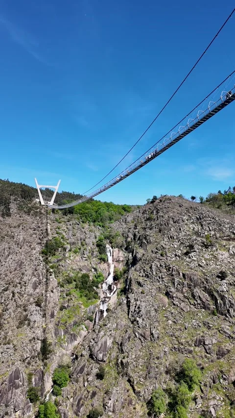 Long suspension bridge over a high waterfall in a mountain canyon 库存影片 332368757
