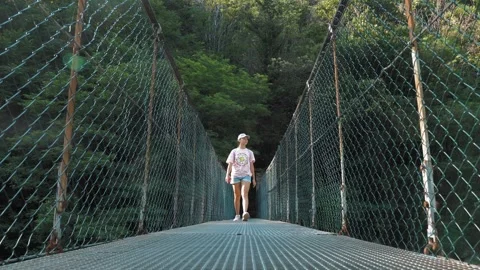 Long suspension bridge over a mountain river in a picturesque green forest among Stock Footage 255161336