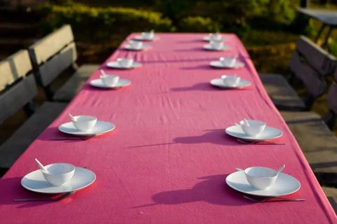 On a long table are plates with cups and cutlery. Stock Photos