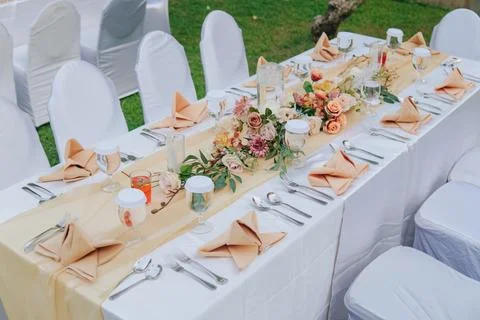 Long table with white table cloth and an elegant floral arrangement in the .. Stock Photos