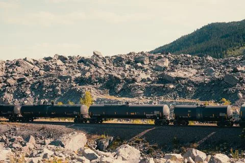 Long tanker train moving along the tracks by the rocky mountainous region. Stock Photos