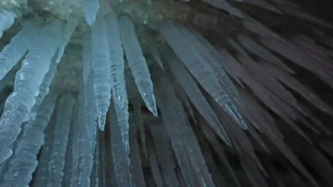 Long tapering white icicles hang on ceiling inside ice cave, frozen stalactites Stock Footage 166567223