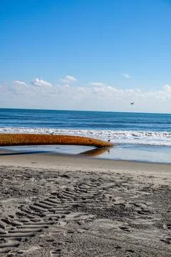 Long thick rusty pipe running along wet beach sand and entering the ground Stock Photos