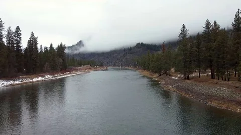 Long tracking shot over wide river toward train bridge with mountain shrouded Stock Footage 125054178