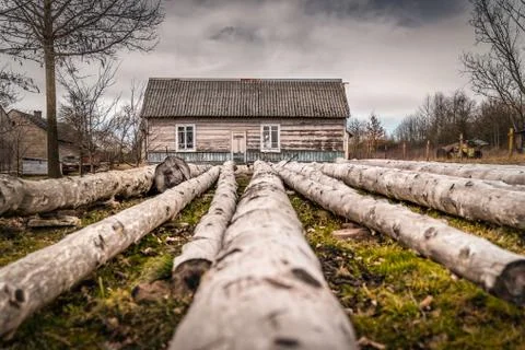 Long tree logs in front of rustic, abandoned and weathered house in countrysi Stock Photos